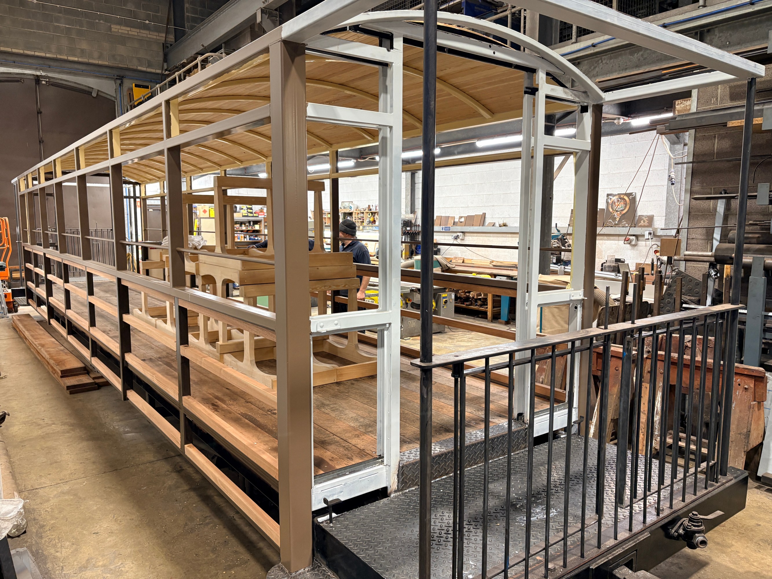 Partially constructed wooden tram in a workshop with metal framing and stairs.