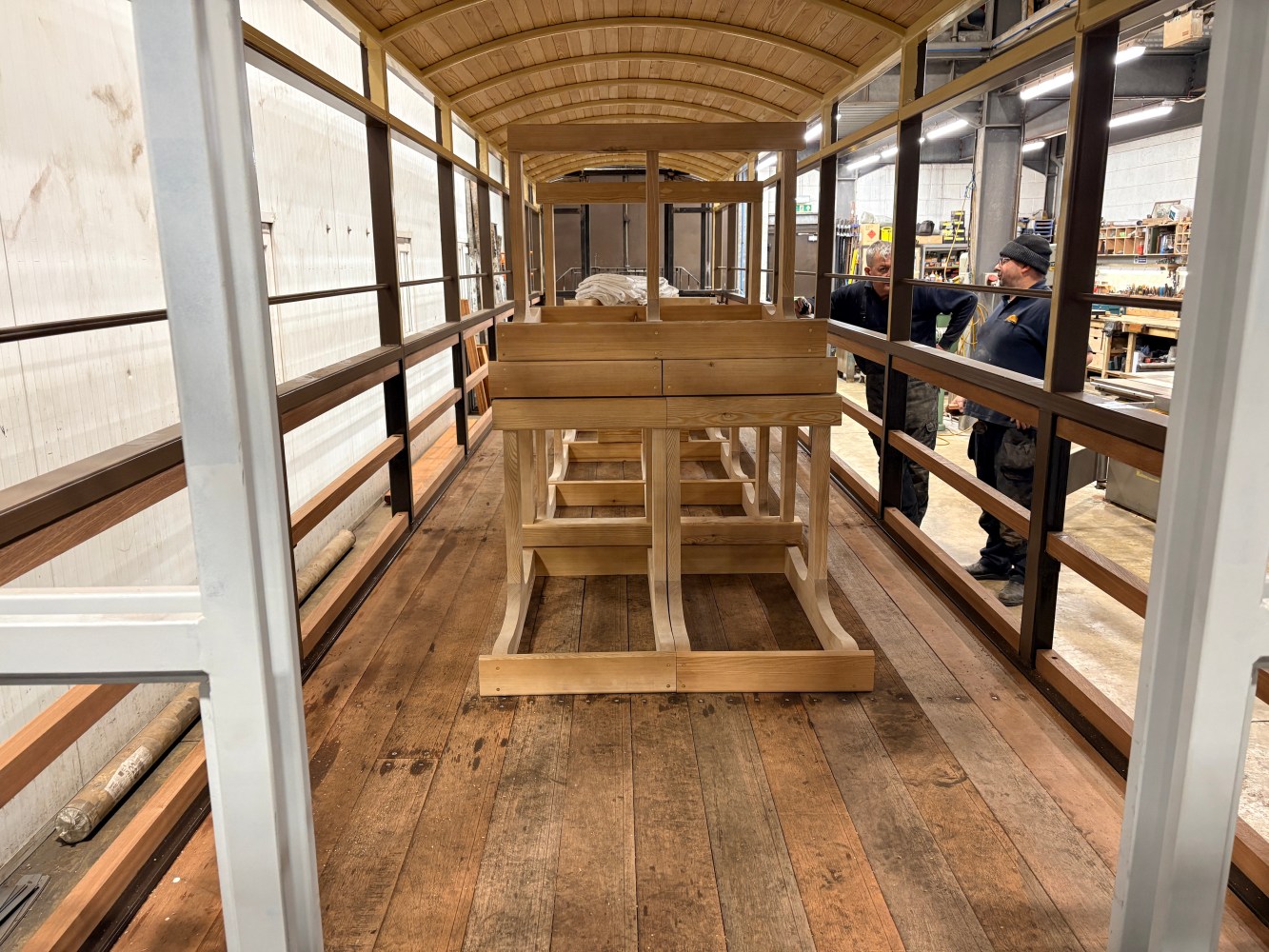 Interior of a partially constructed wood and metal tram with workers in the background.