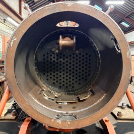 View inside a large, empty, cylindrical metal boiler in an industrial workshop.