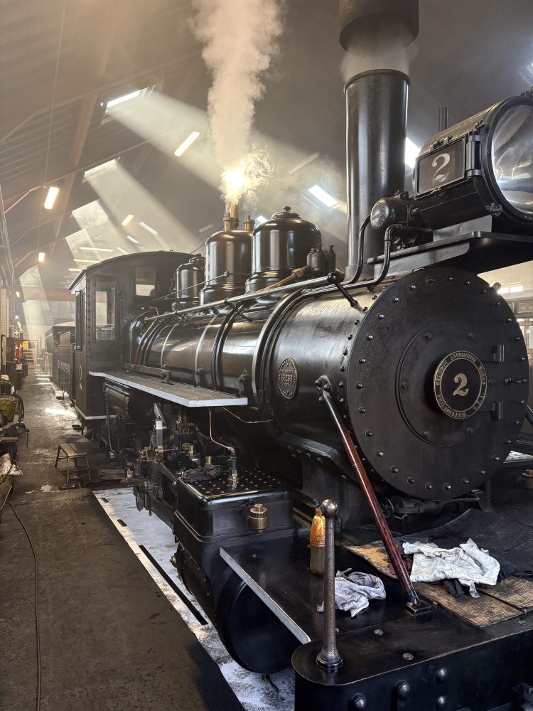 Steam locomotive in a dimly lit warehouse with steam emitting from the top.