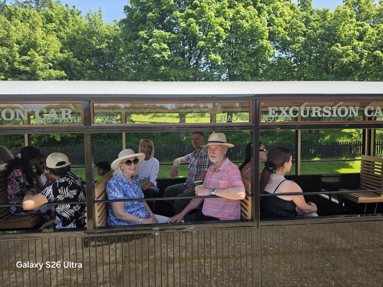 People sitting in an open train carriage on a sunny day.