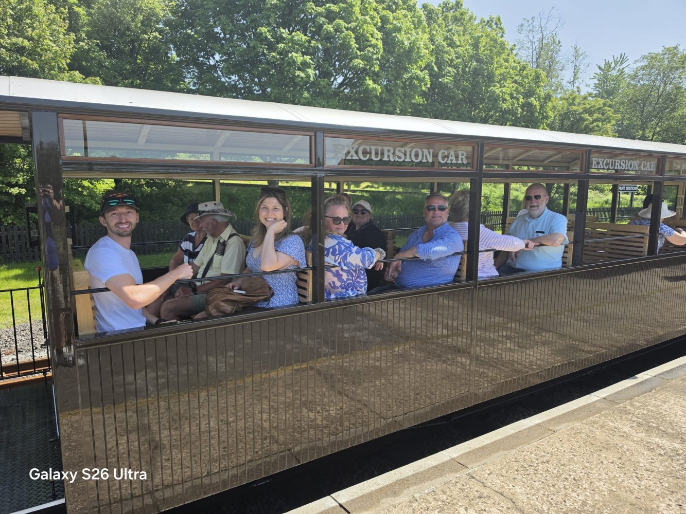 Group of people seated in an open excursion train car on a sunny day.