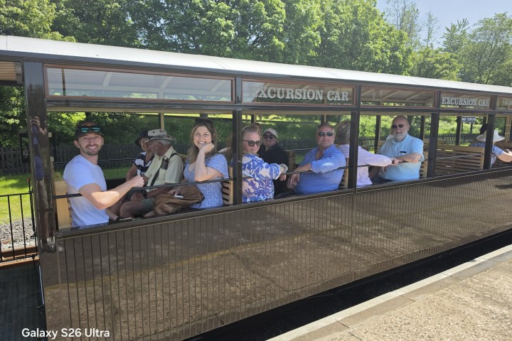 Group of people seated in an open excursion train car on a sunny day.