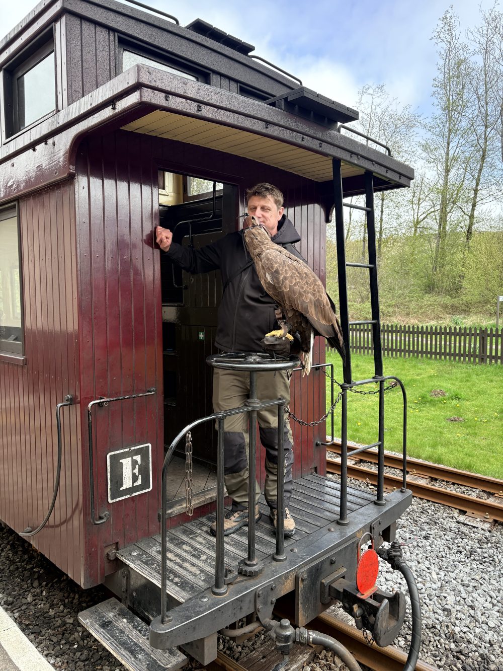 Person standing on a vintage train car holding a large bird.