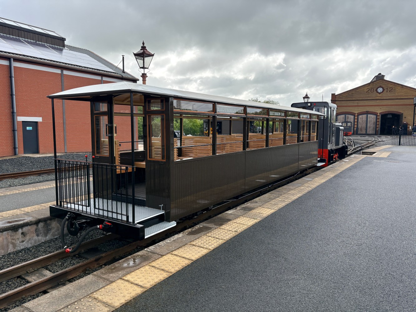 Vintage tram on tracks near a brick building under a cloudy sky.