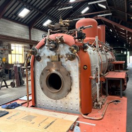 Industrial workshop with a large vintage boiler and tools scattered around.