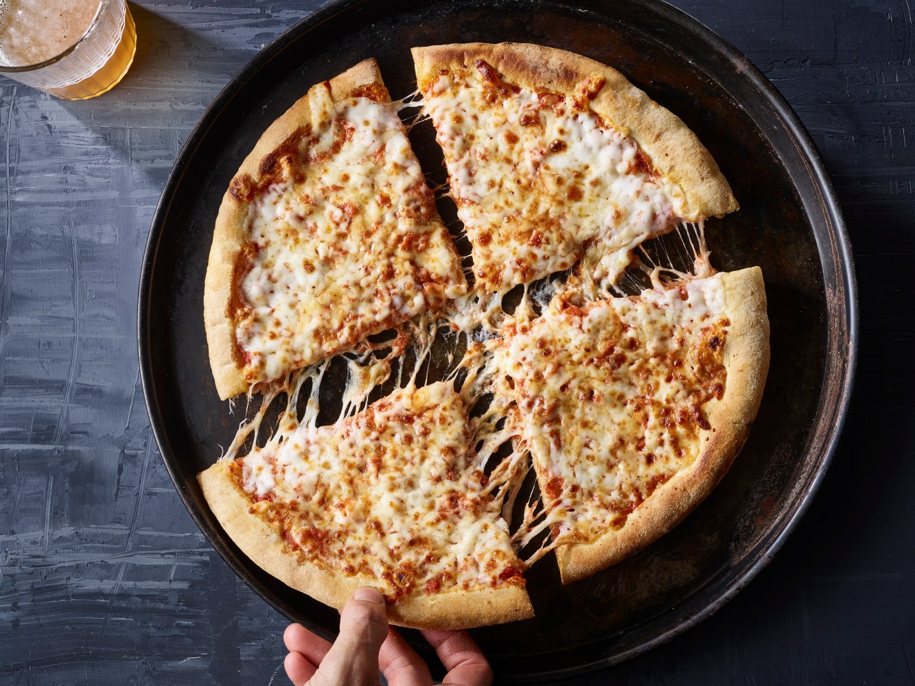 Hand picking a cheese pizza slice from a pan.