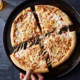 Hand picking a cheese pizza slice from a pan.