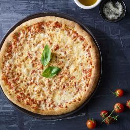 Cheese pizza with basil, bowl of olive oil, salt, and cherry tomatoes on a dark background.