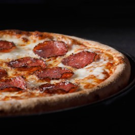 Pizza with melted cheese and pepperoni on a dark background.